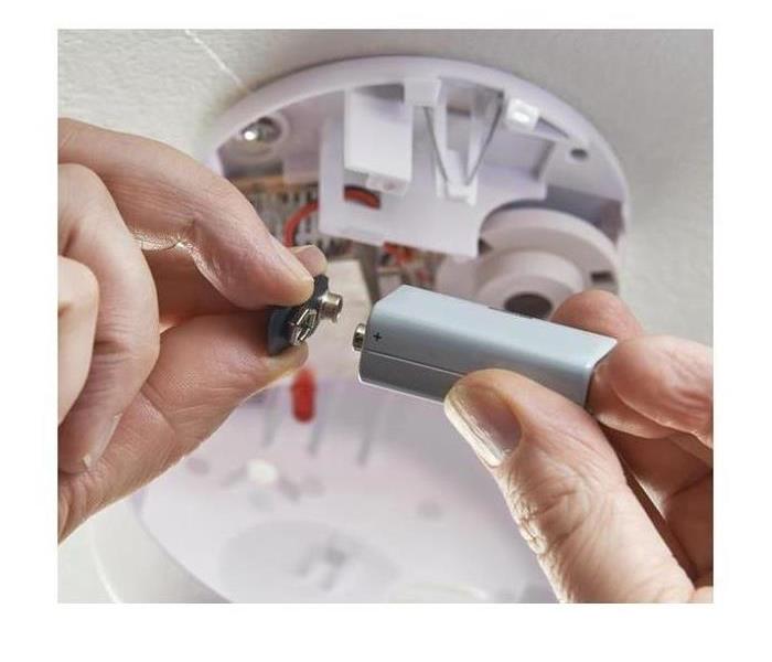 A person changing the battery in their smoke alarm