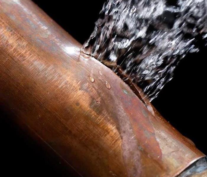 A piece of copper pipe with water spewing out of a break in the pipe