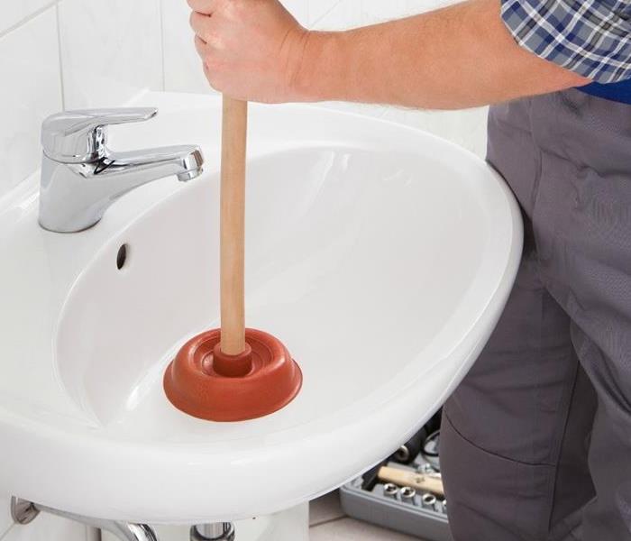 Homeowner using a plunger to clear a clog in the pipe