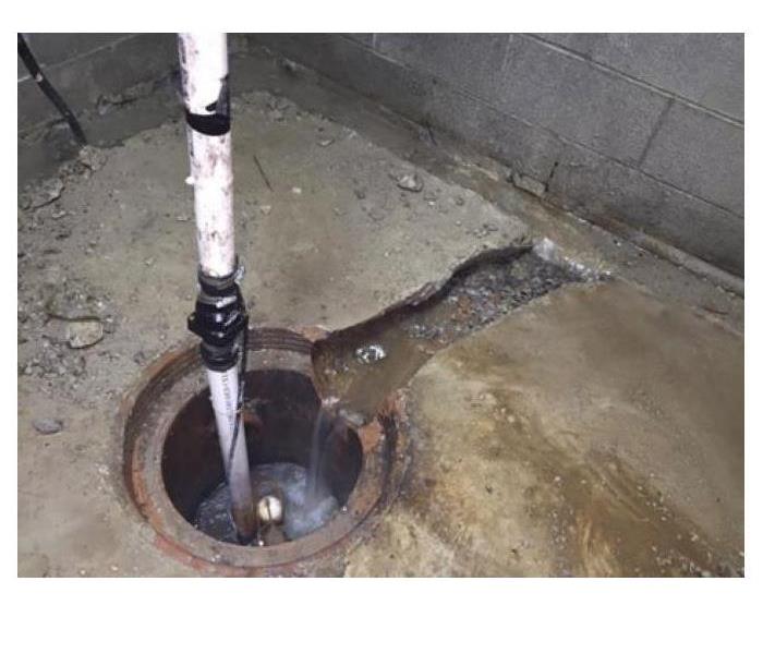 Water running into a sump pump pit in the basement of a building.