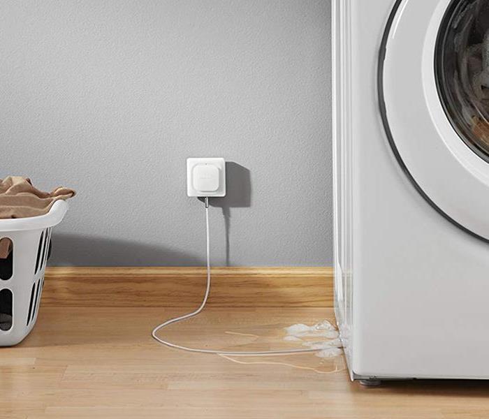 A water senor plugged into a wall with a wire running along the floor to the washing machine.